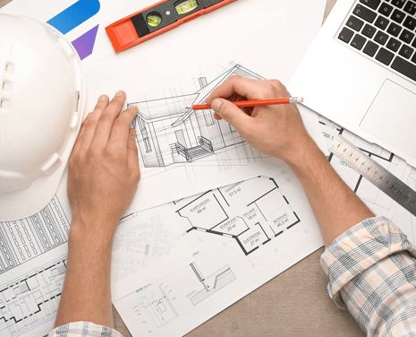 Man hands drawing house plans with construction helmet and laptop on the side